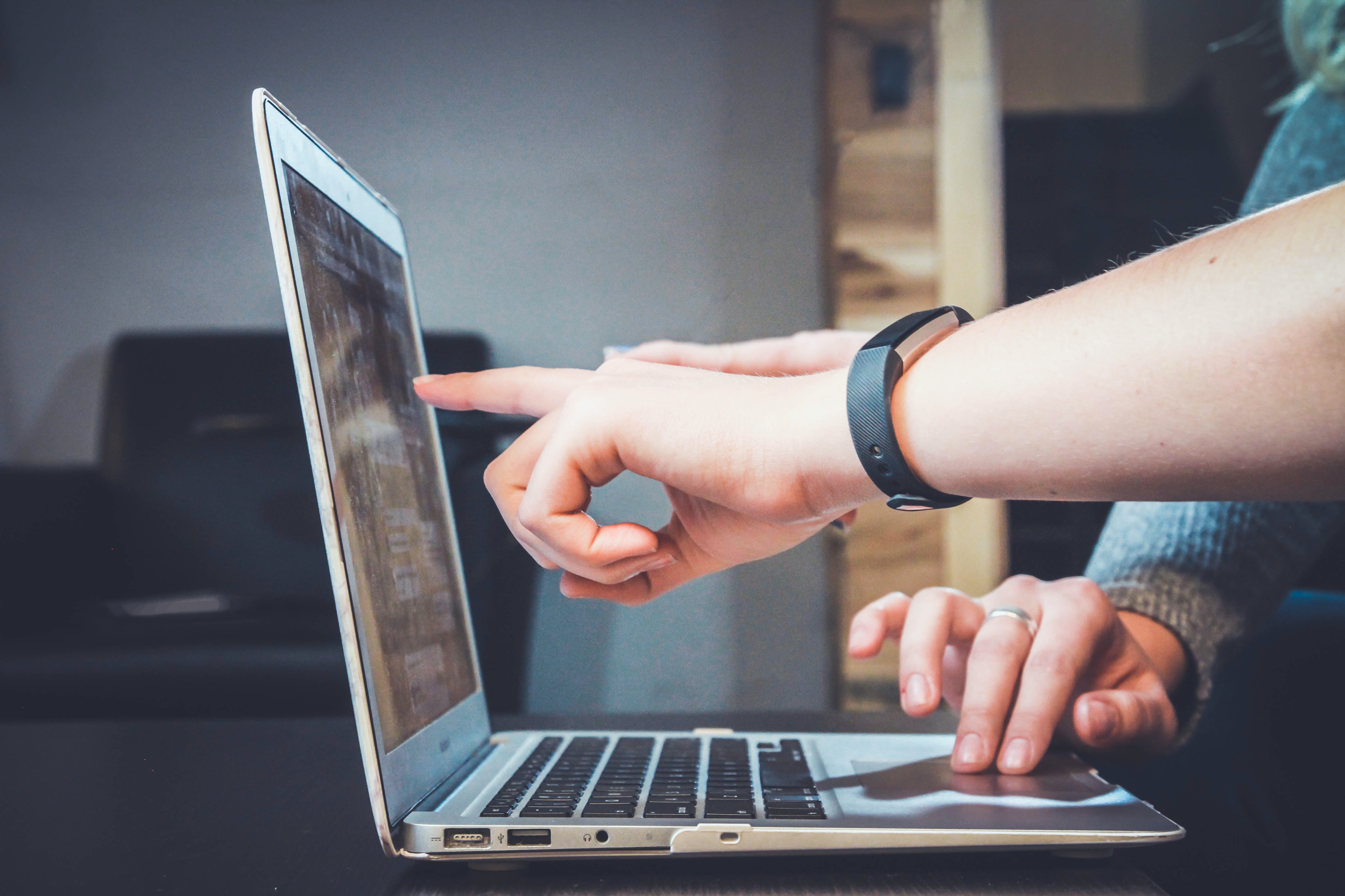 Image of laptop with woman's arm pointing to the screen. Man's hand on the mouse.
