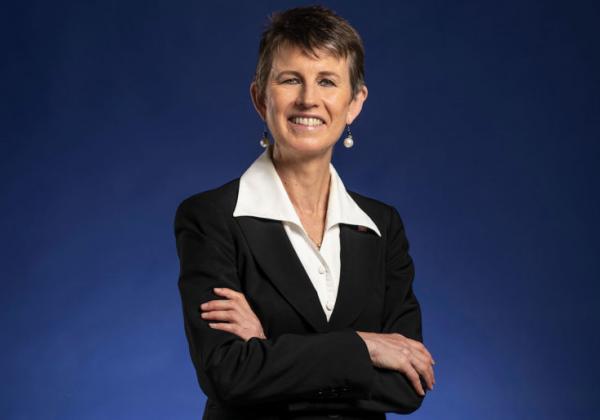 Engineers Australia CEO Bronwyn Evans in a white shirt a black blazer standing with arms folded in front of a blue background. 